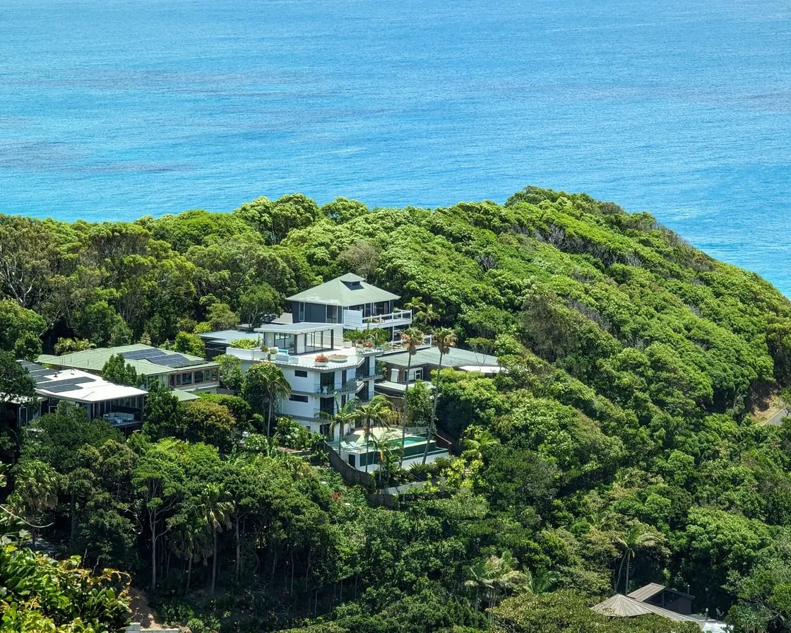 Luxury white multi-level Australian beach house with a pool and palm trees on a green headland above a turquoise ocean