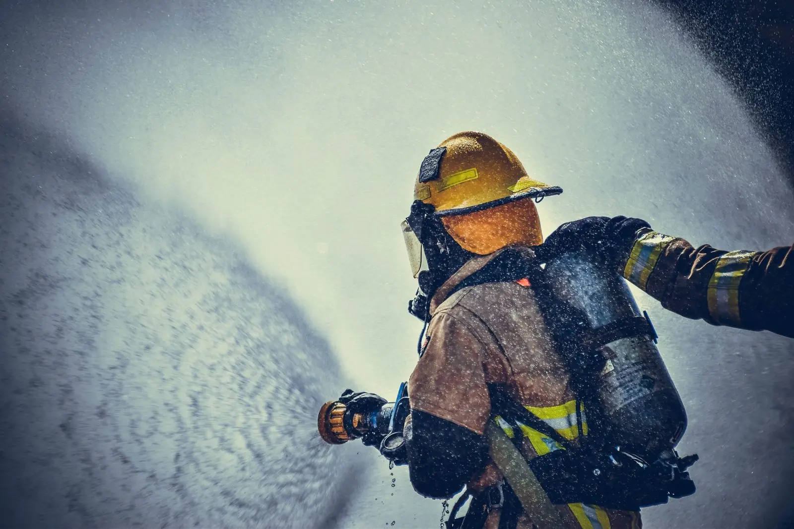 Firefighter in a yellow helmet spraying a fire hose