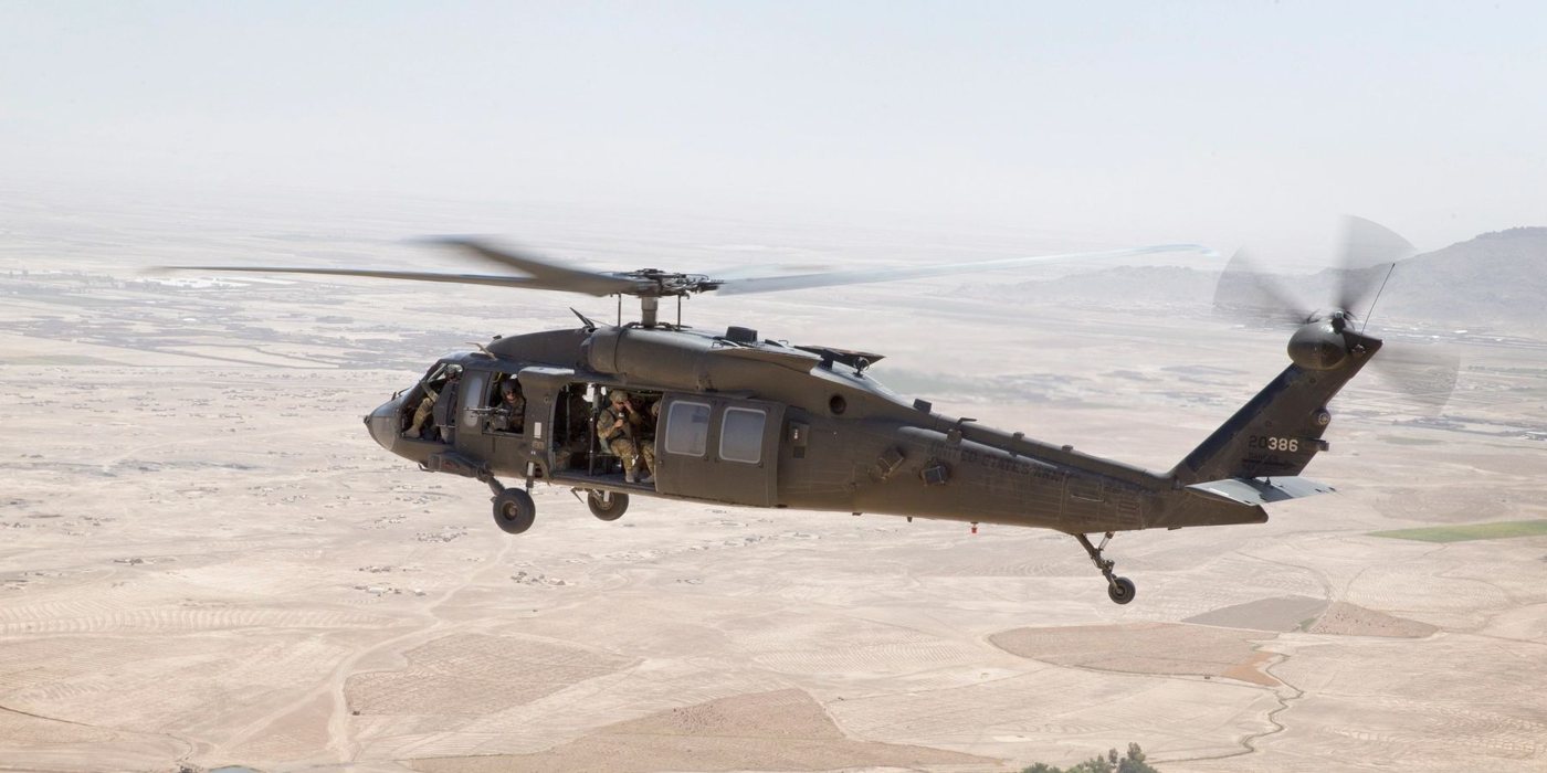 Military Black Hawk helicopter with crew aboard flying over arid terrain