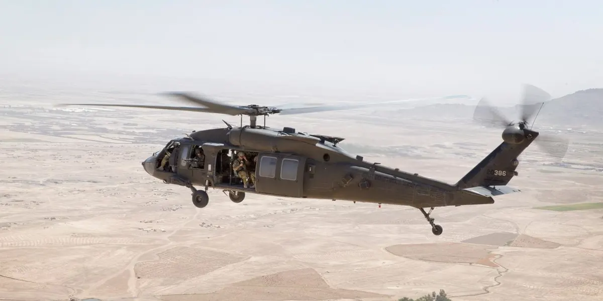 Military Black Hawk helicopter with crew aboard flying over arid terrain