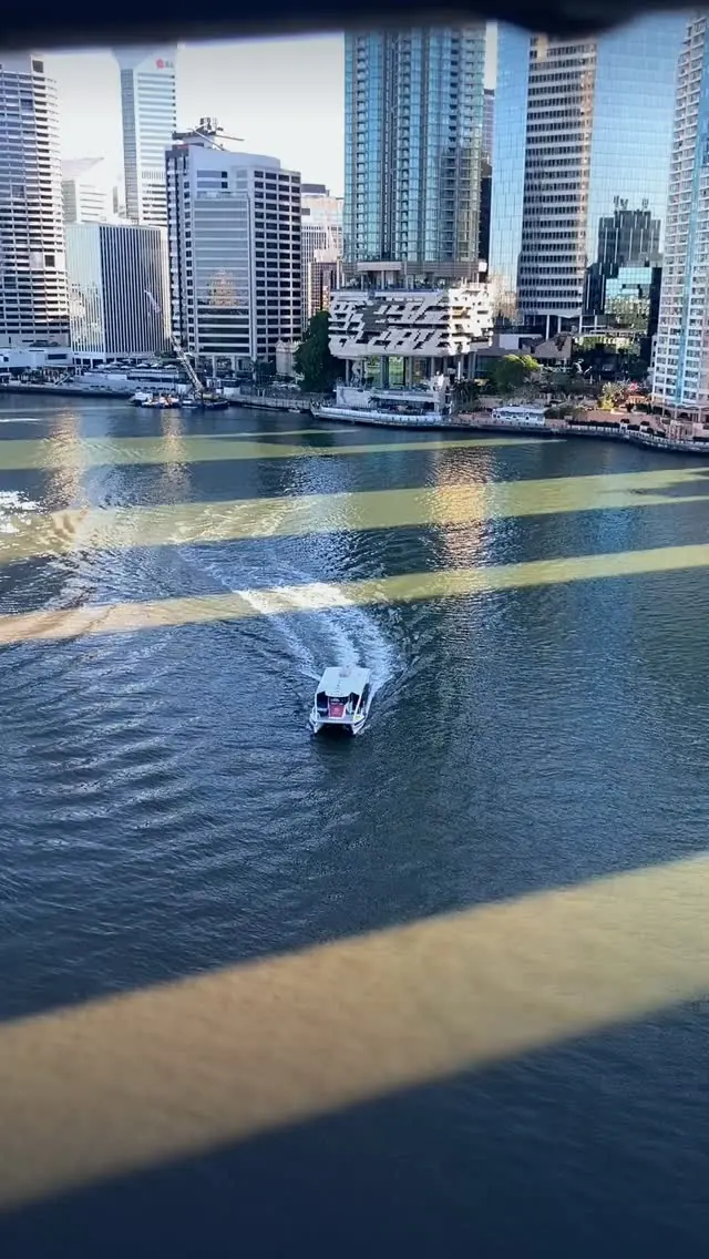 The Brisbane River and city towers seen through the shadows of a bridge
