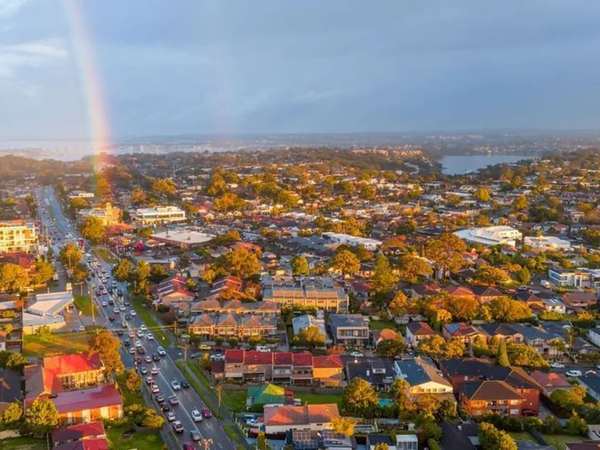 Rainbow over an Australian suburb with tree-lined streets and rooftops at sunset