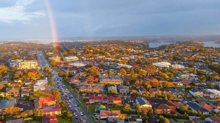 Rainbow over an Australian suburb with tree-lined streets and rooftops at sunset