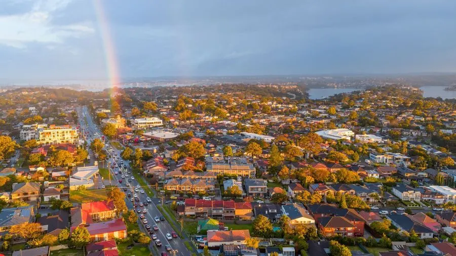 Rainbow over an Australian suburb with tree-lined streets and rooftops at sunset